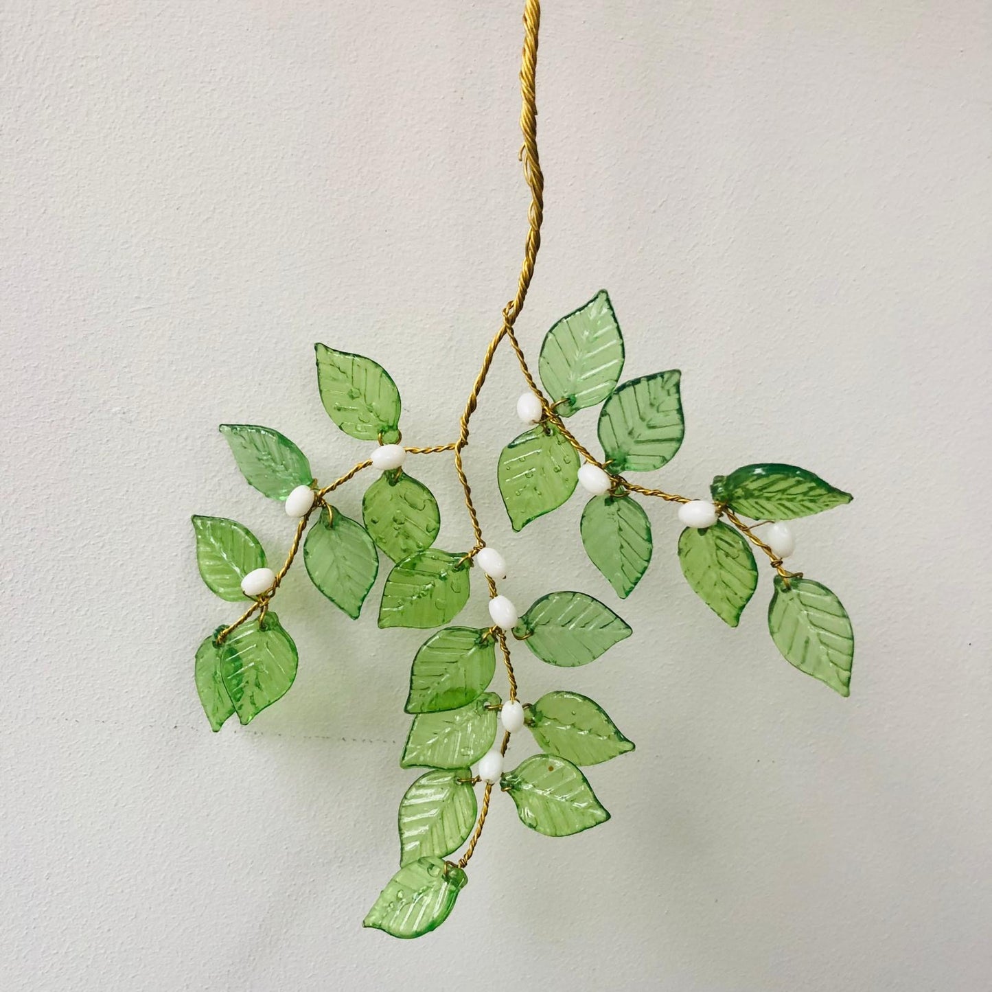 Decorative leaf garland with green leaves and white beads on a light background
