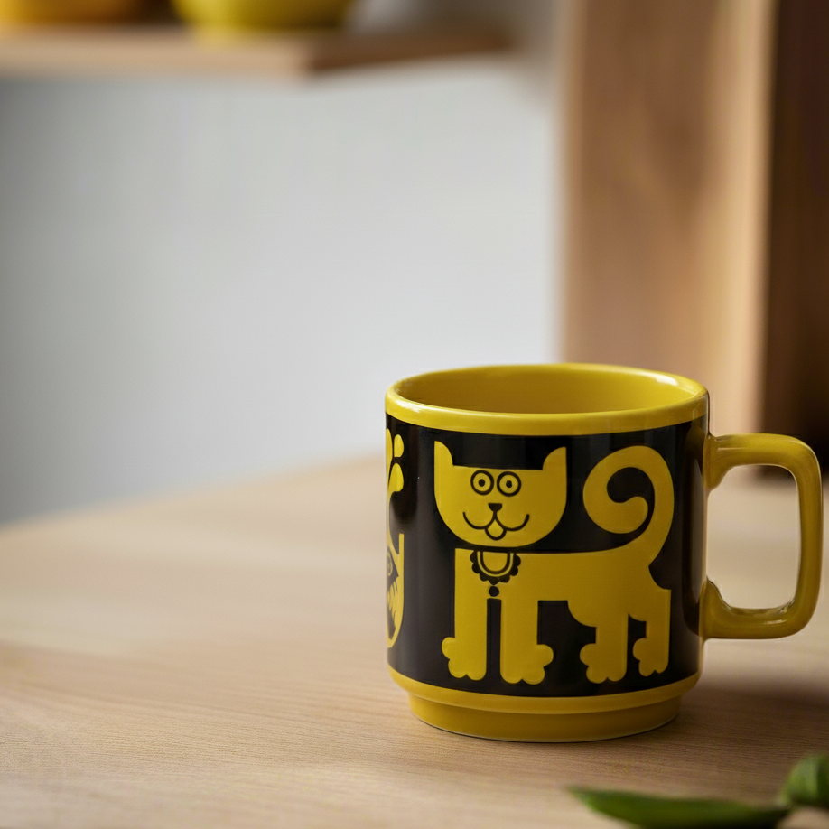 Yellow mug with a black cat design on a wooden surface