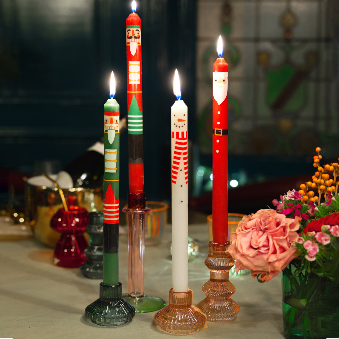 Decorative candles with festive designs on a table with flowers and other items.